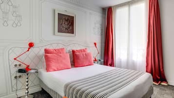 A hotel room with a bed, red lamps, a framed artwork, and a window with red curtains.