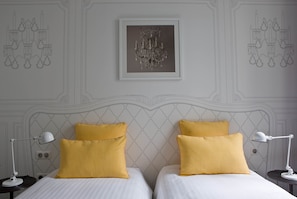 Ein Doppelbett mit zwei gelben Kissen, einem weißen Kopfteil und einer rahmenartigen Chandelüster an der Wand.