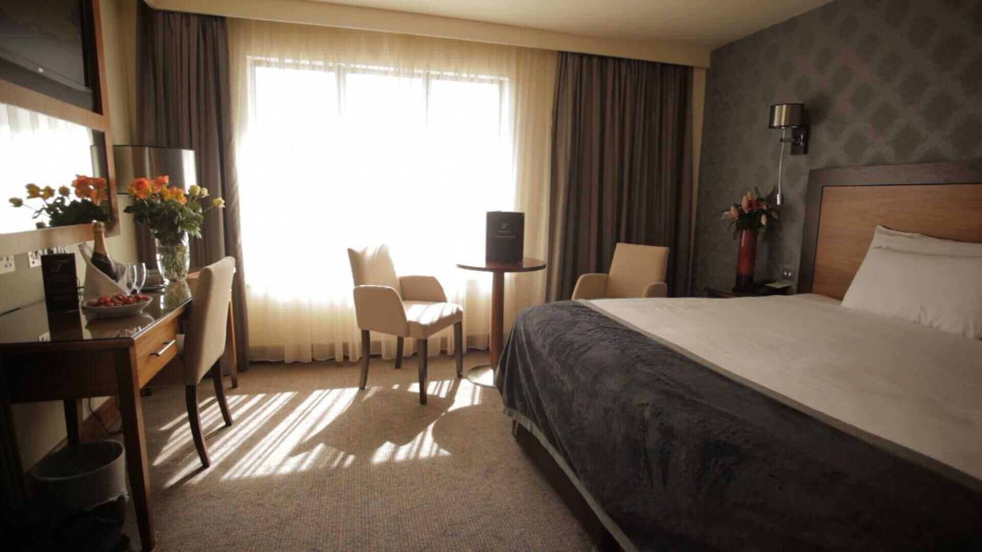 A hotel room with a large bed, a desk with a chair, a small table, and a TV.