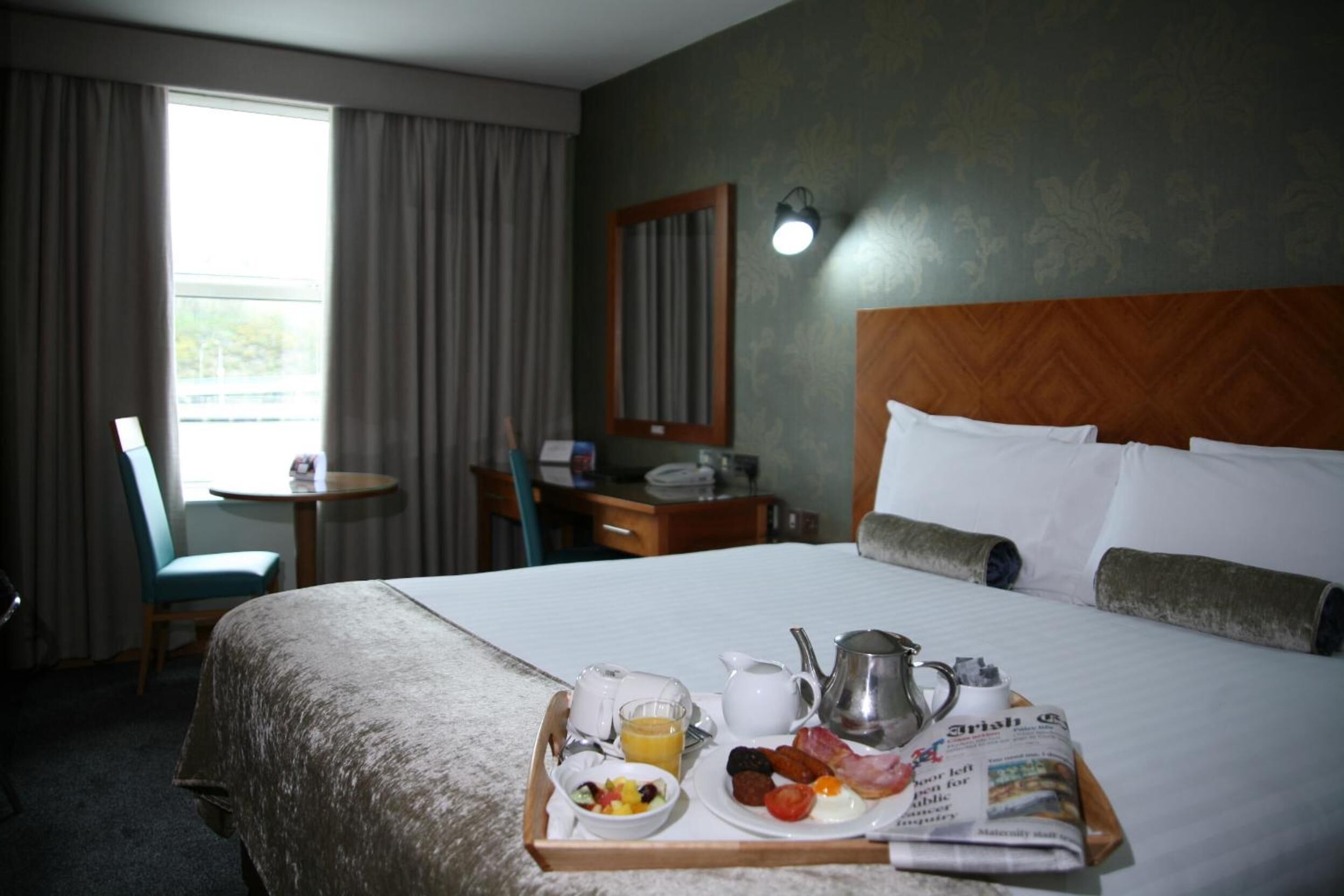 A hotel room with a bed, breakfast tray, newspaper, and a view of the outdoors.