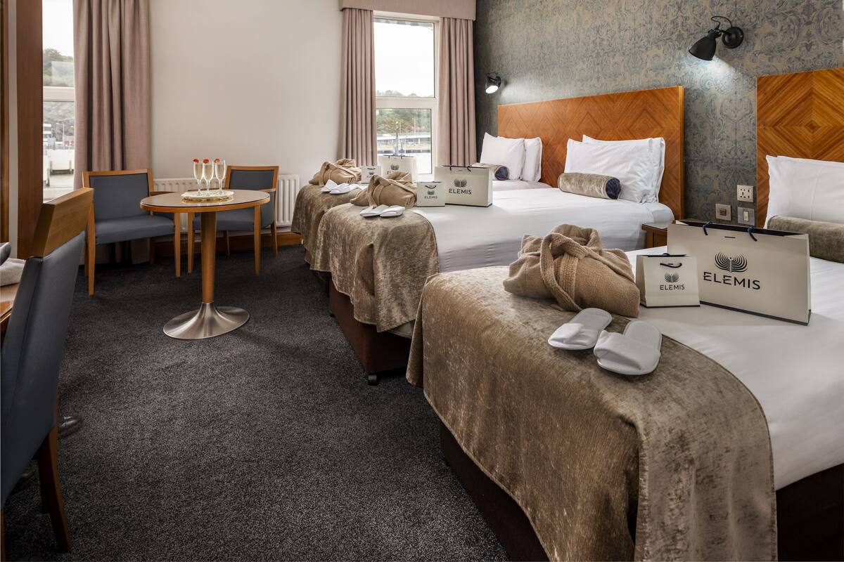 Ein Hotelzimmer mit zwei Betten, einem Esstisch und Blick auf die Stadt.