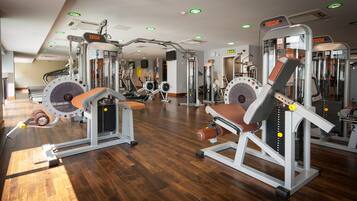 Uma academia com diversos equipamentos de exercício, piso de madeira e luminárias no teto.