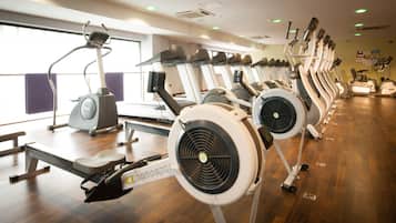 Un gimnasio con numerosas cintas de correr y bicicletas estáticas, suelo de madera y ventanas amplias que permiten la entrada de luz natural.