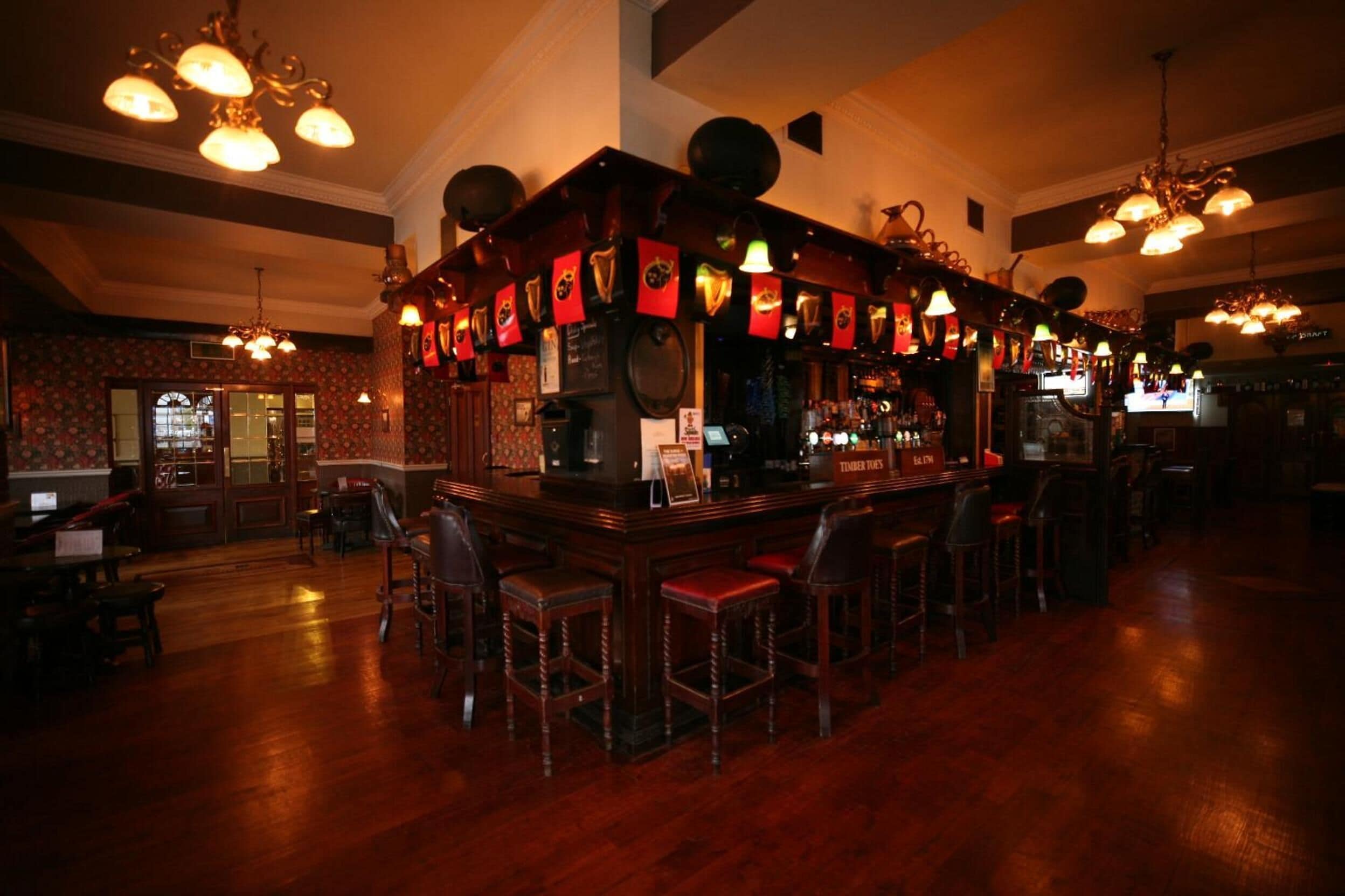 Un área de bar con taburetes de madera, una barra con menú y luces colgantes.