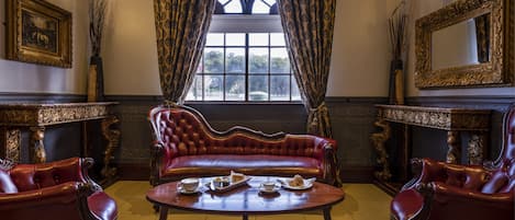A room with a red leather sofa, two armchairs, a wooden coffee table, and a large ornate mirror.