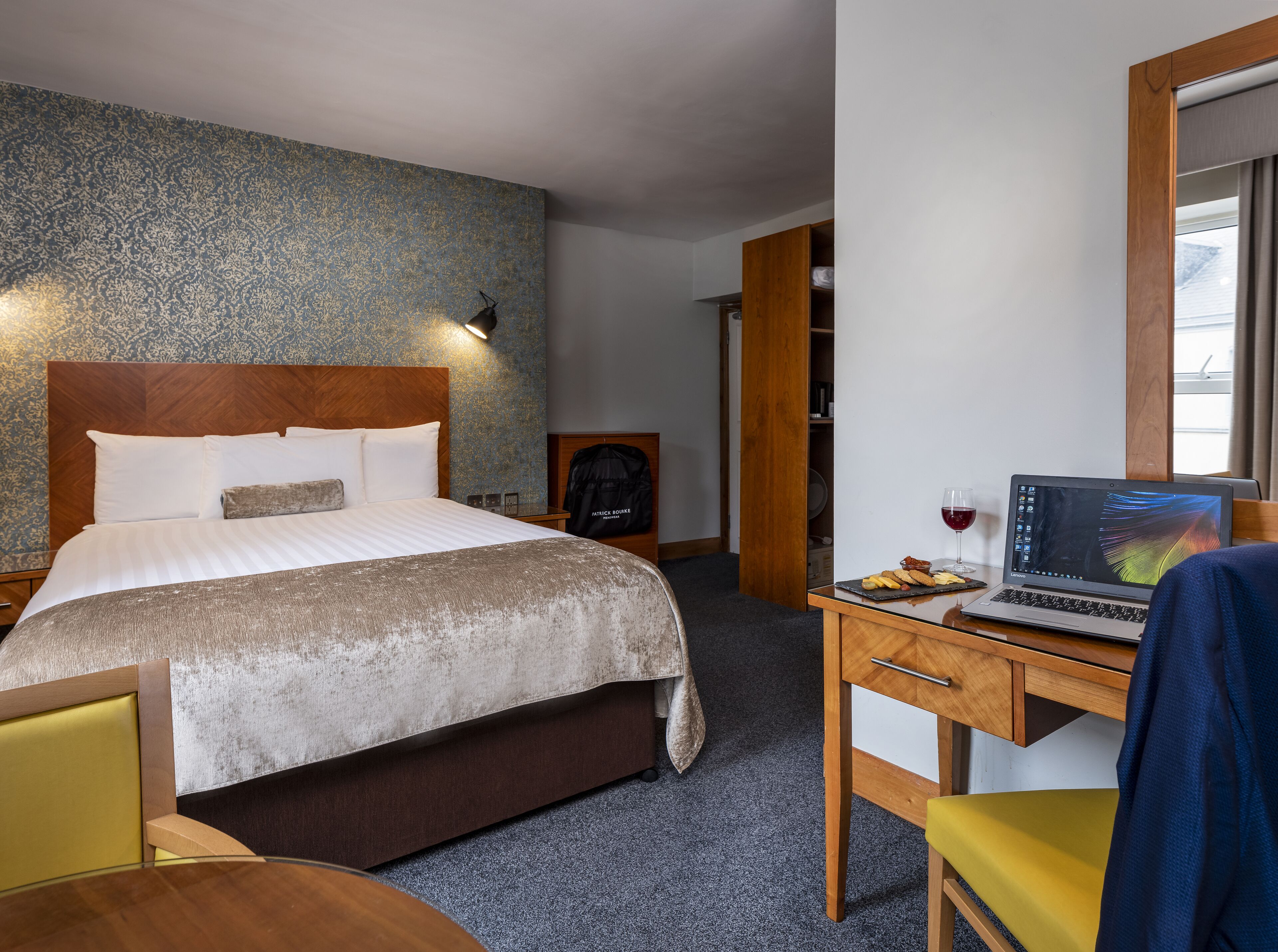 A hotel room with a bed, a desk with a laptop, a chair, and a wardrobe.