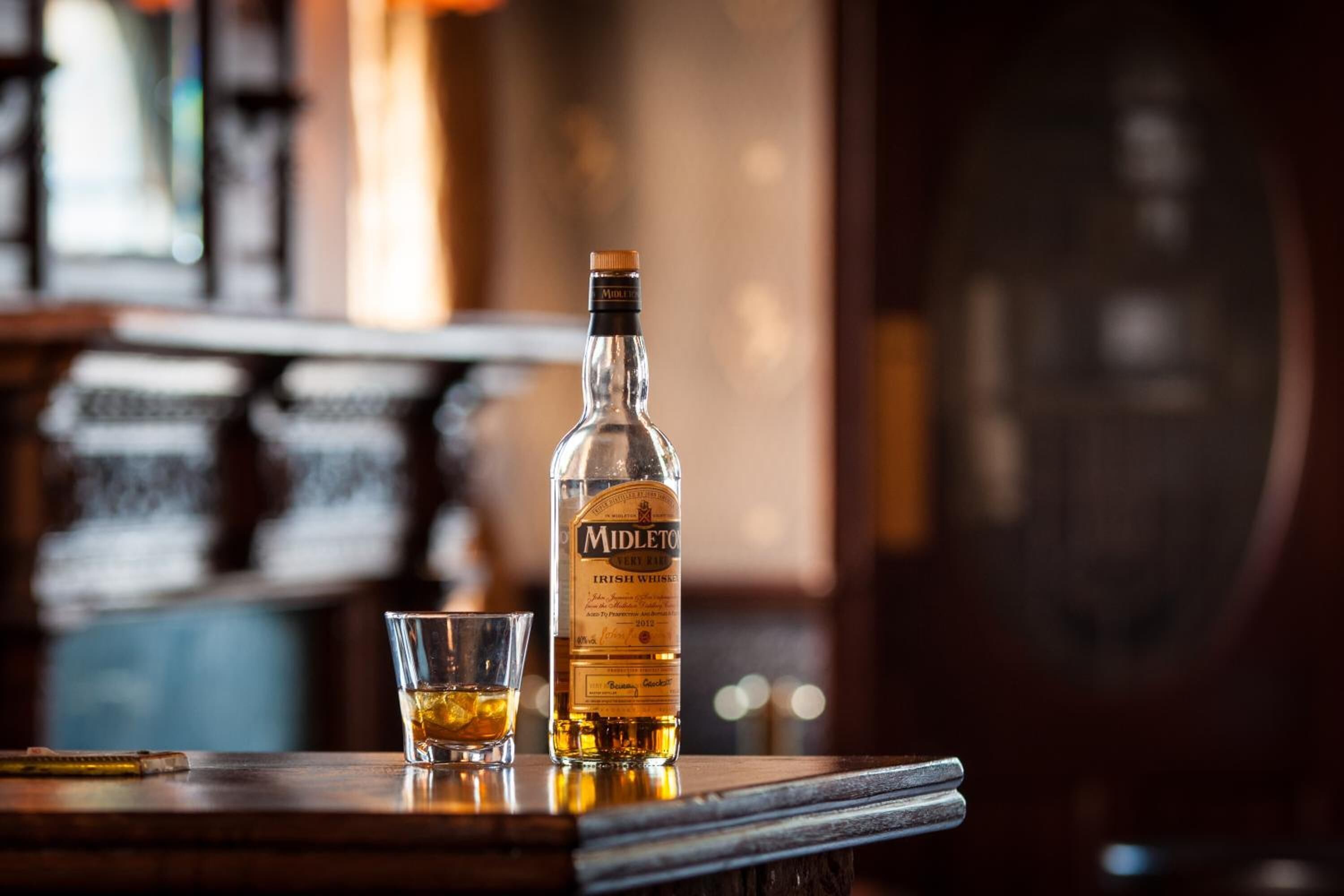 Una botella de whiskey irlandés Midleton y un vaso sobre una barra de madera.