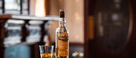 A bottle of Midleton Irish Whiskey and a glass on a wooden bar counter.