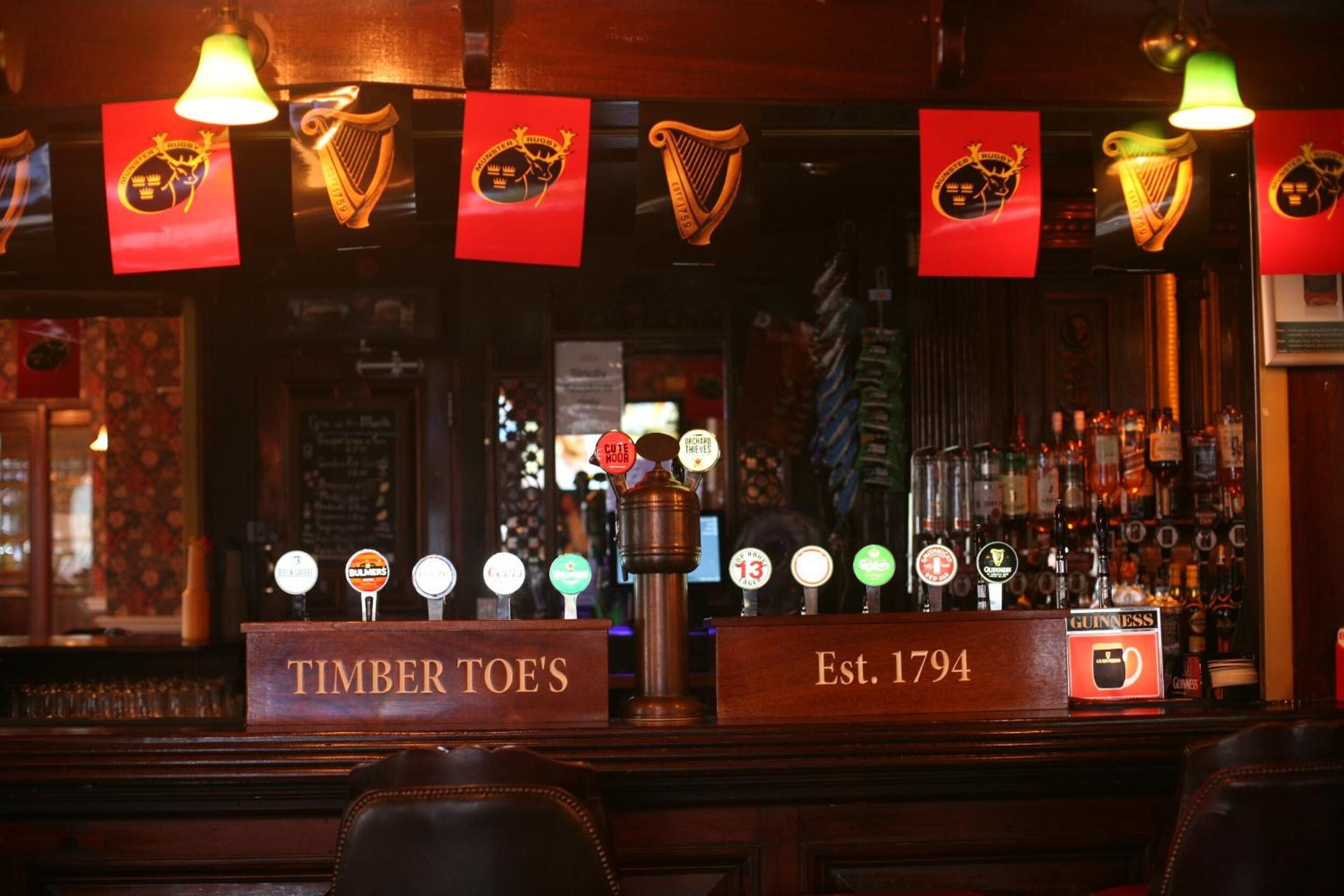 Un bar amb un taulell de fusta, diverses aixetes de cervesa i un cartell que indica 'Timber Toe's' i 'Est. 1794'.