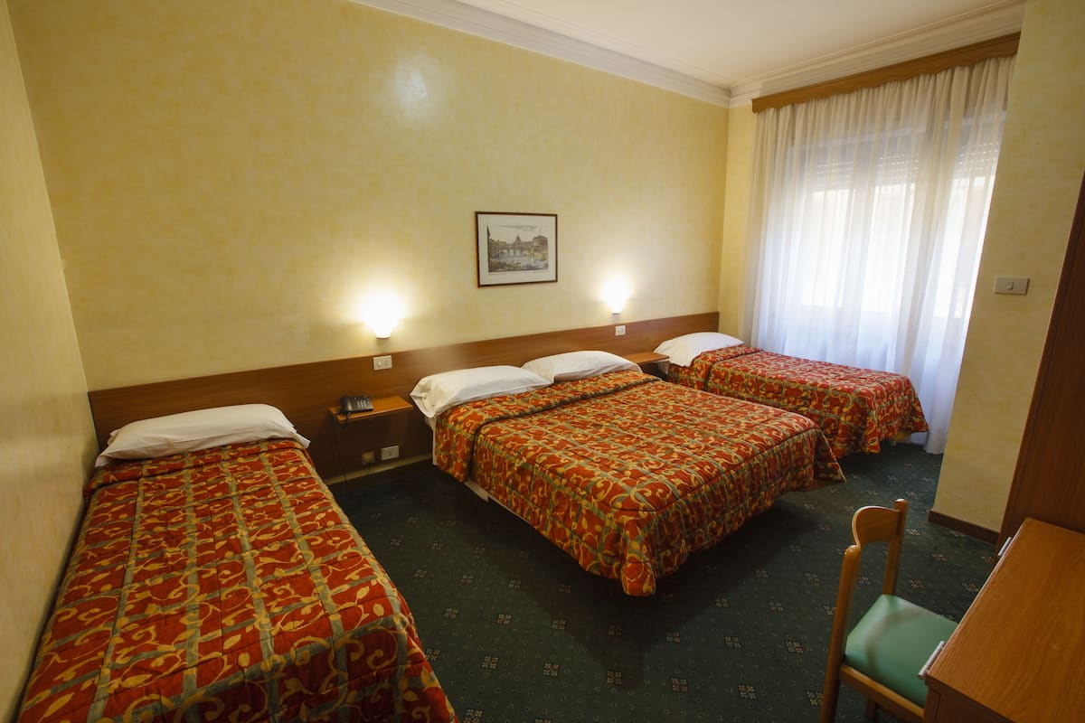 A hotel room with two single beds, a wooden headboard, a small table, a chair, and a framed picture on the wall.