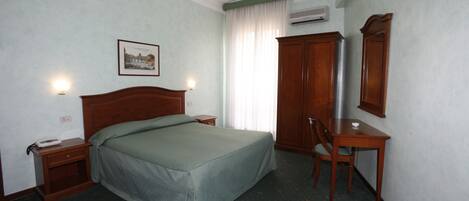 Een hotelkamer met een bed, nachtkastje, stoel, bureau en een lijst aan de muur.