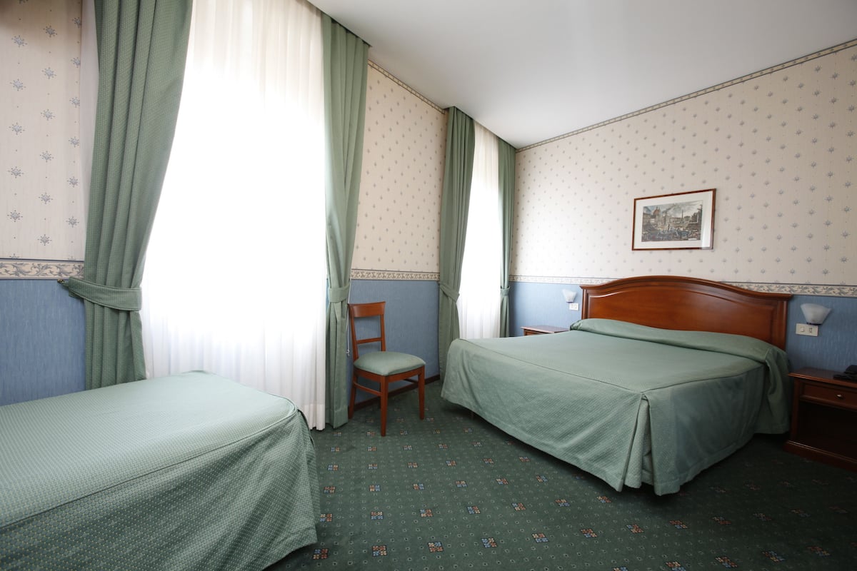 A hotel room with two single beds, a chair, a nightstand, and a framed picture on the wall.