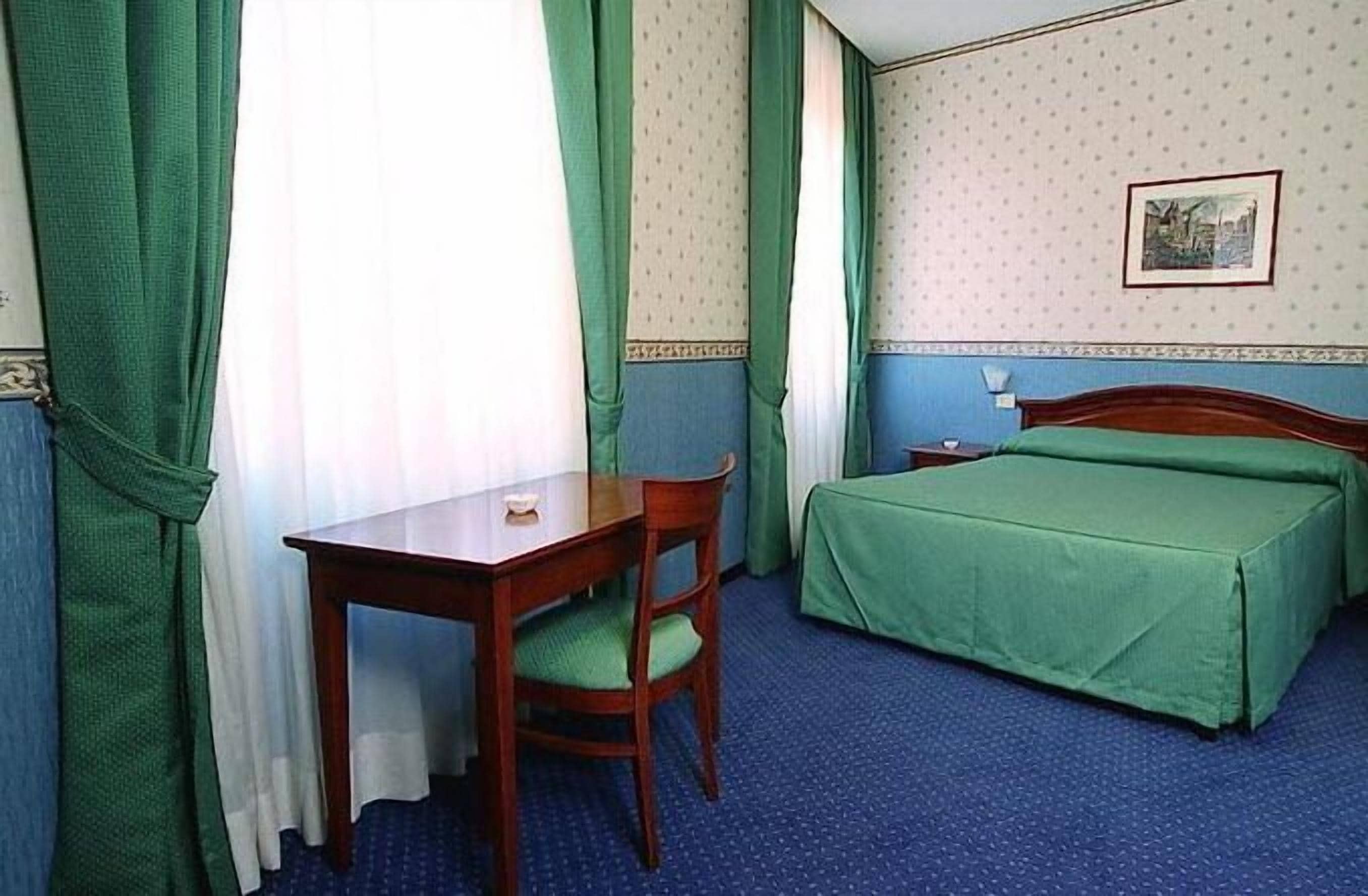 Et hotelværelse med en enkelt seng, et skrivebord med stol og et lille bord.