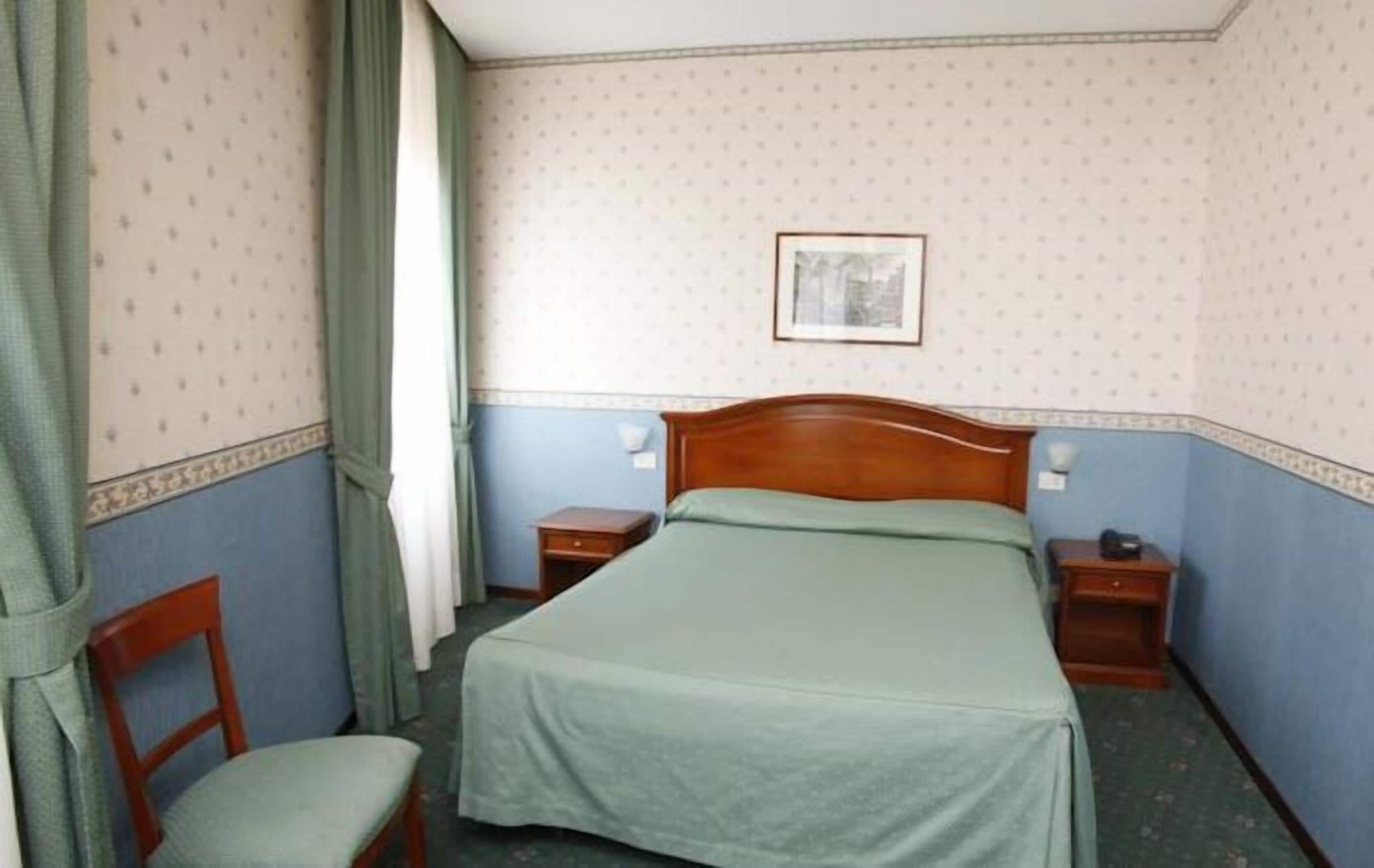 Un lit simple avec une tête de lit en bois, deux tables de chevet, une chaise et un tableau encadré au mur.