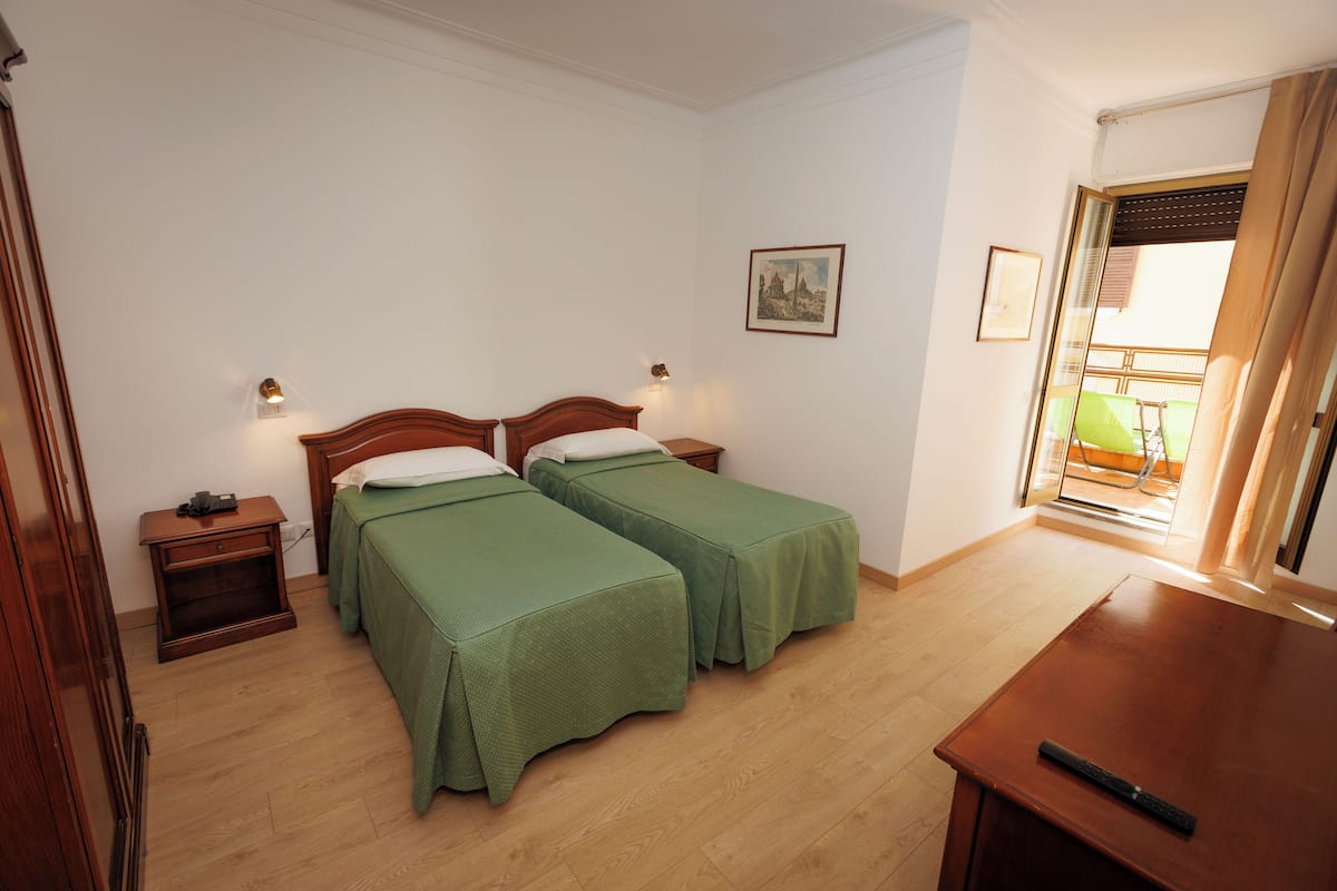 A room with two single beds, a wooden nightstand, a small table, and a window with a view.