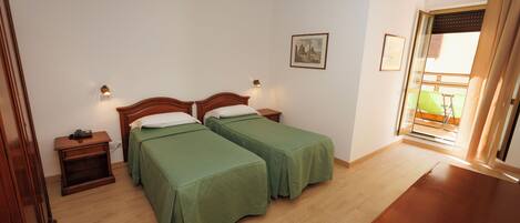 A room with two single beds, a wooden nightstand, a small table, and a window with a view.