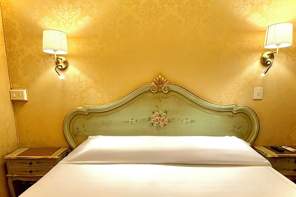 A hotel room with a large bed, two wall-mounted lamps, and a floral headboard.