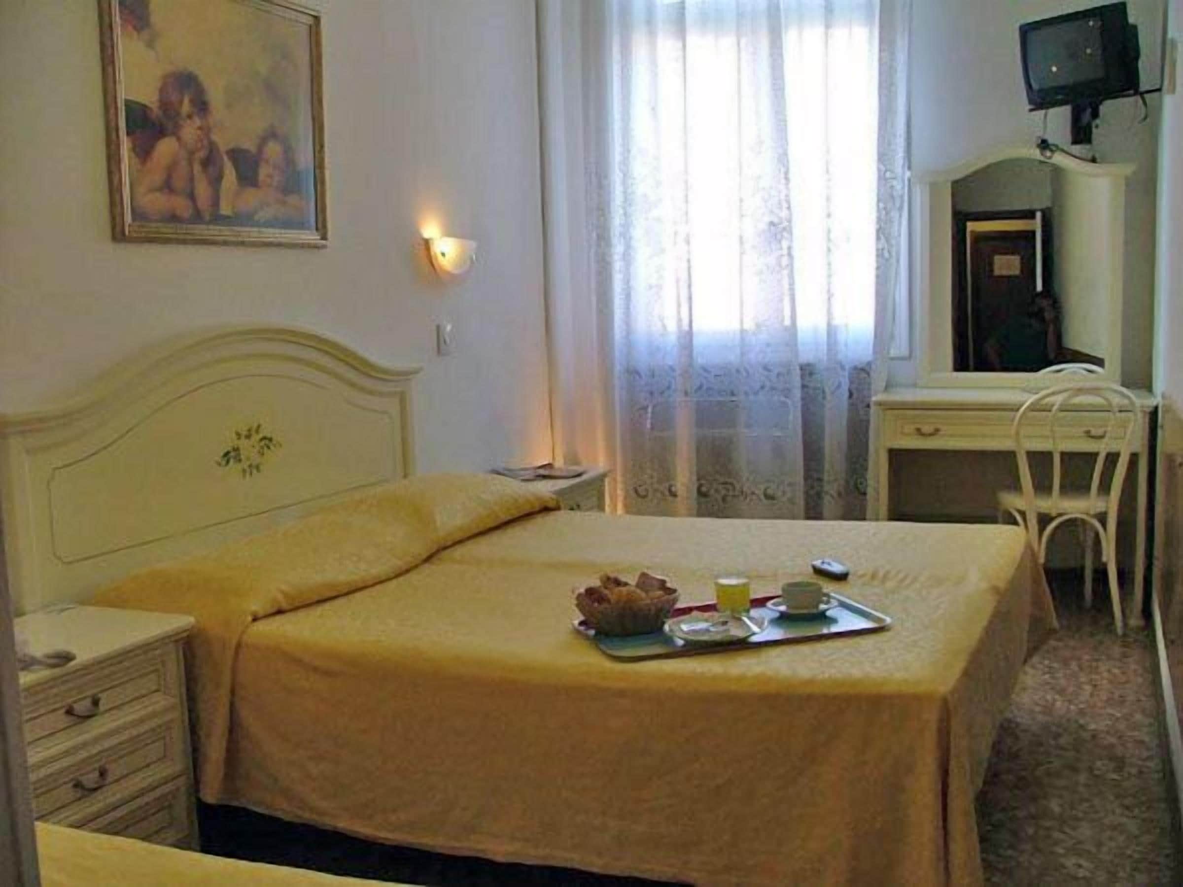 A hotel room with a bed, a bedside table, a desk, and a chair.