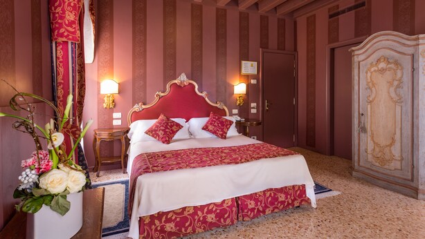 A large bed with a red headboard, two bedside lamps, a wooden nightstand, and a large wardrobe. - Hotel Tiziano (Venice)