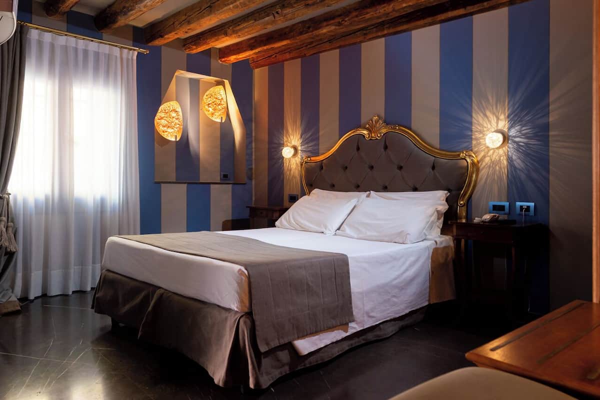 A hotel room with a large bed, striped wallpaper, and two wall-mounted lamps.