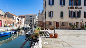 A waterfront hotel with a canal, potted plants, and a clear blue sky. - Hotel Tiziano (Venice)