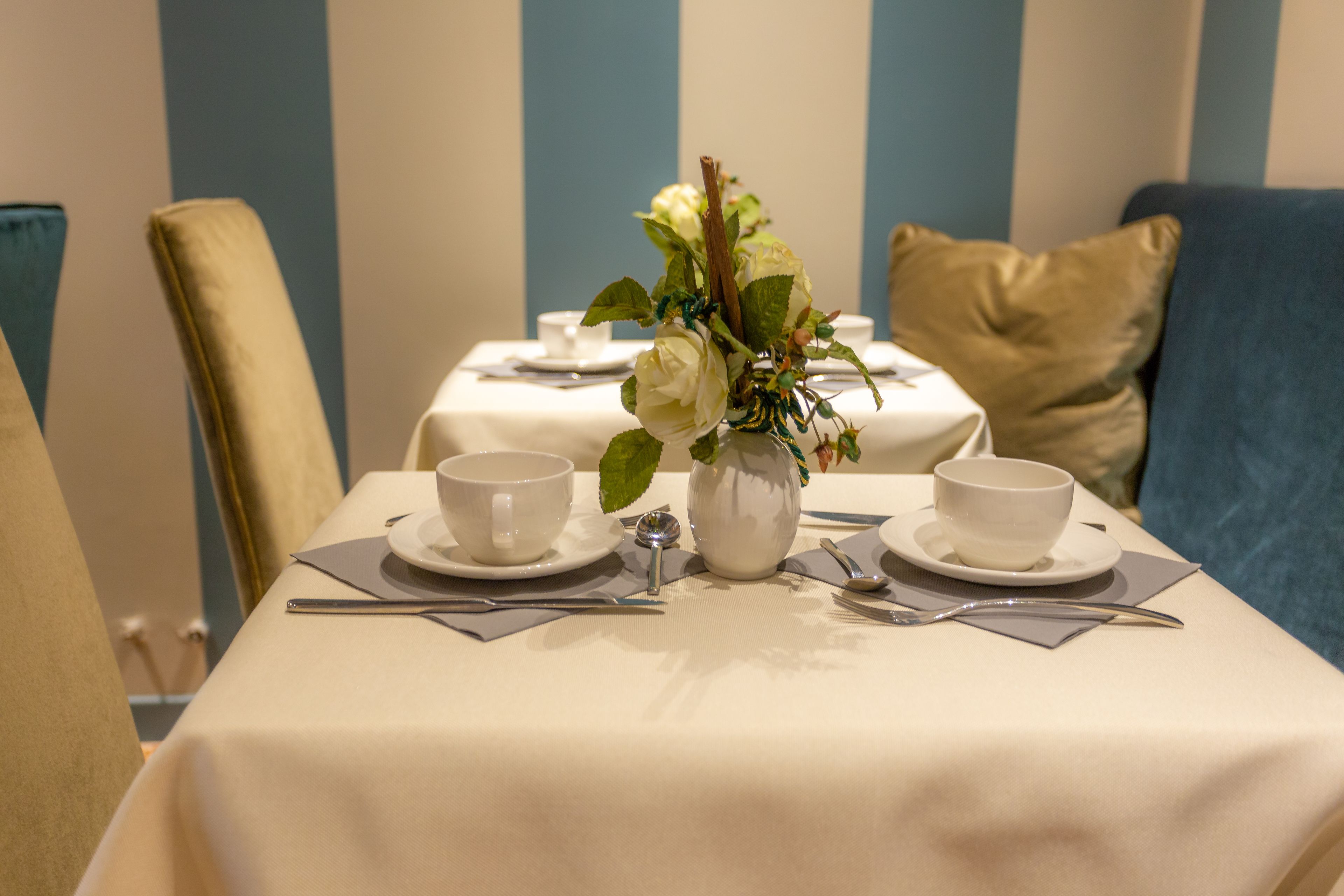 Une table à manger dressée avec de la vaisselle blanche et un vase de fleurs, le tout sur fond de murs à rayures.