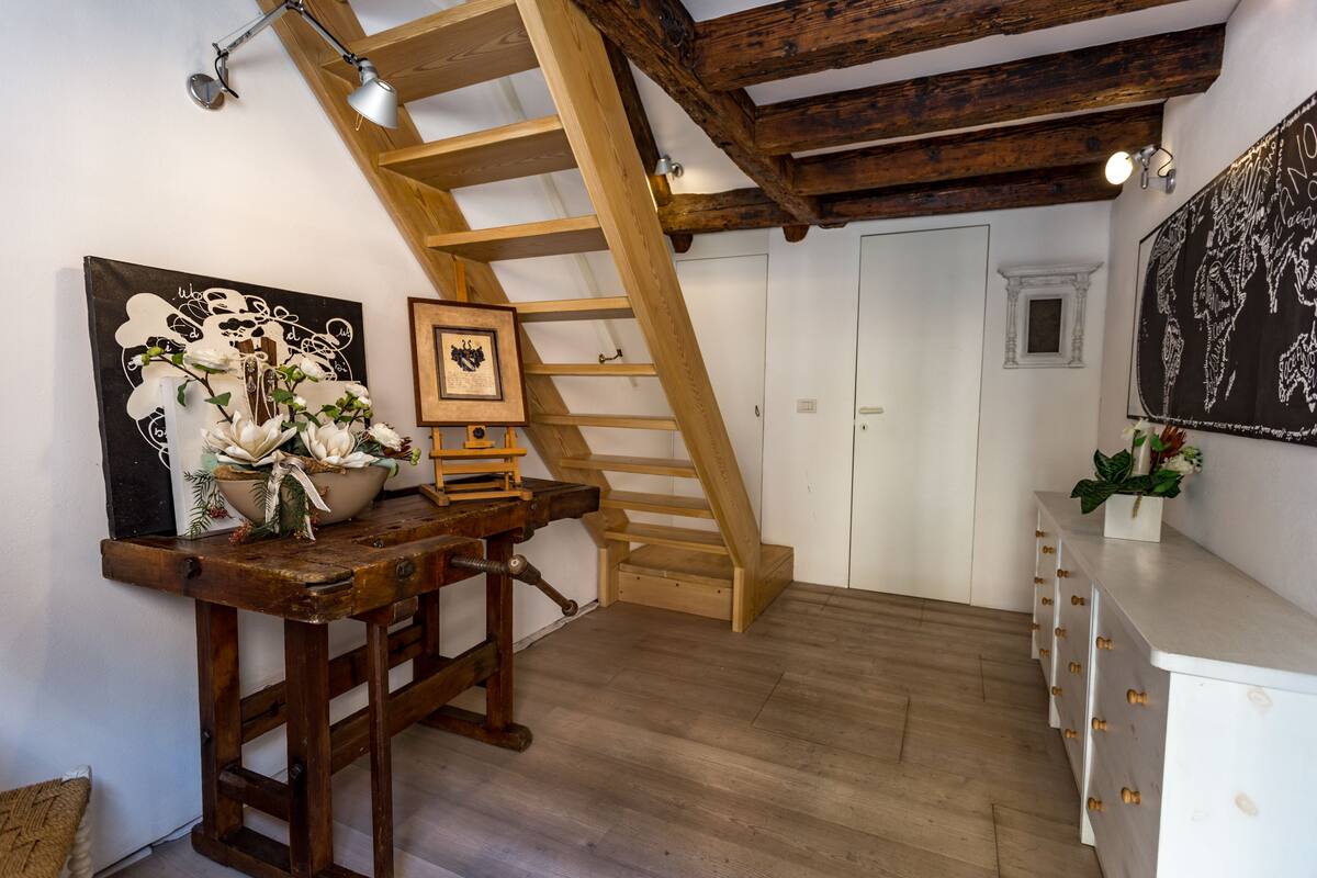 A room with a wooden staircase, a desk with a vase of flowers, and a white dresser.