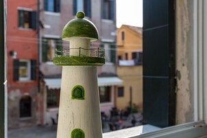 Vihreäkuvuisella ja valkoisella alustalla varustettu majakka, jota katsotaan ikkunasta, ja taustalla näkyy rakennuksia.