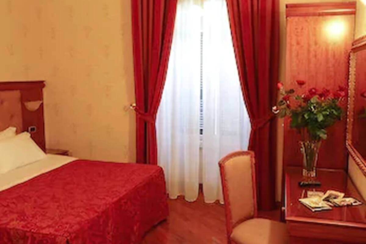 A hotel room with a bed, a desk with a mirror, and a chair.