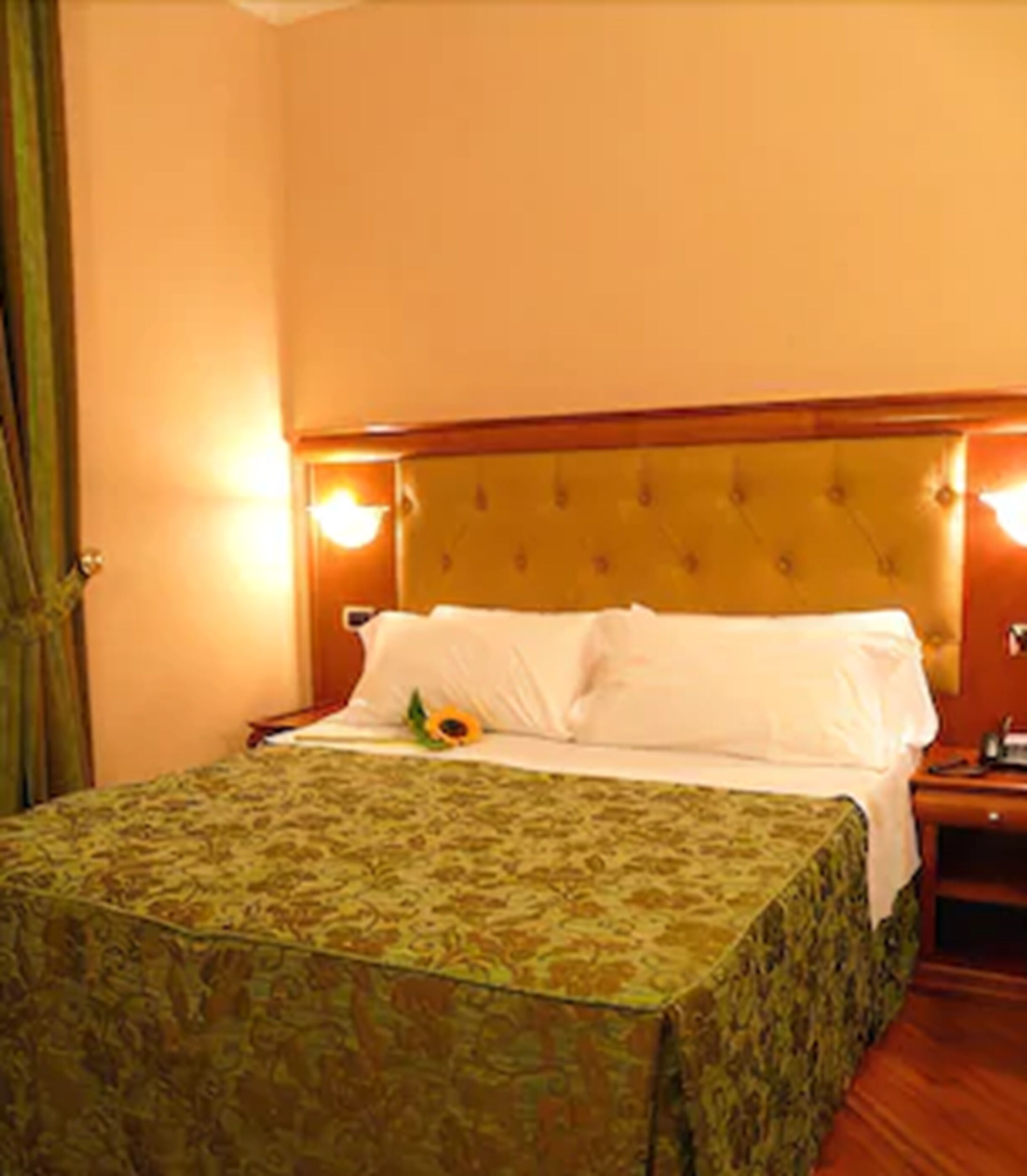 A hotel room with a bed, a nightstand, and a wall-mounted lamp.