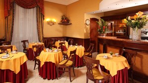 A hotel dining area with round tables covered in yellow tablecloths and red curtains. - Serena Hotel (Rome)