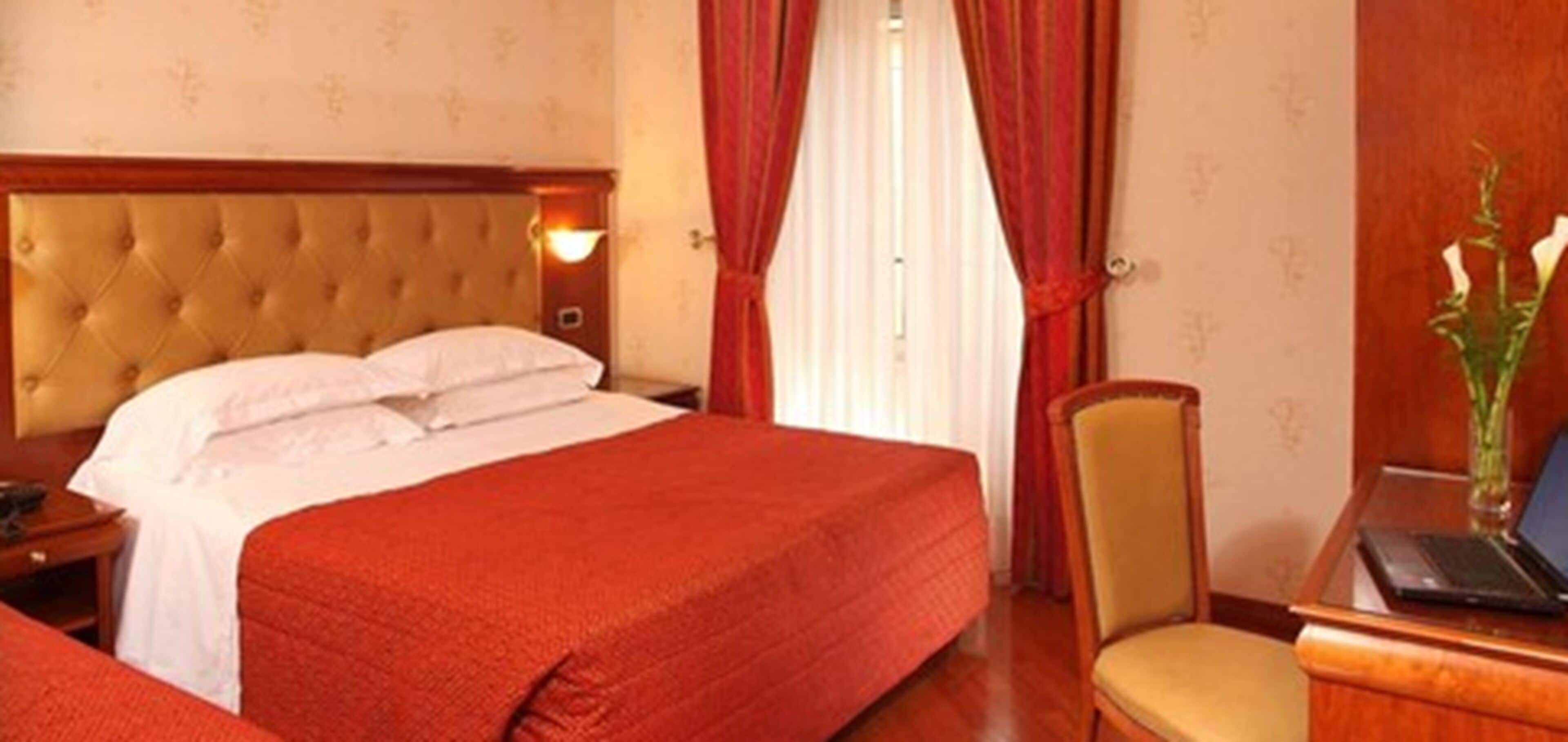 Habitación de hotel con una cama grande, un cabecero de madera, un escritorio con una computadora portátil y una silla.
