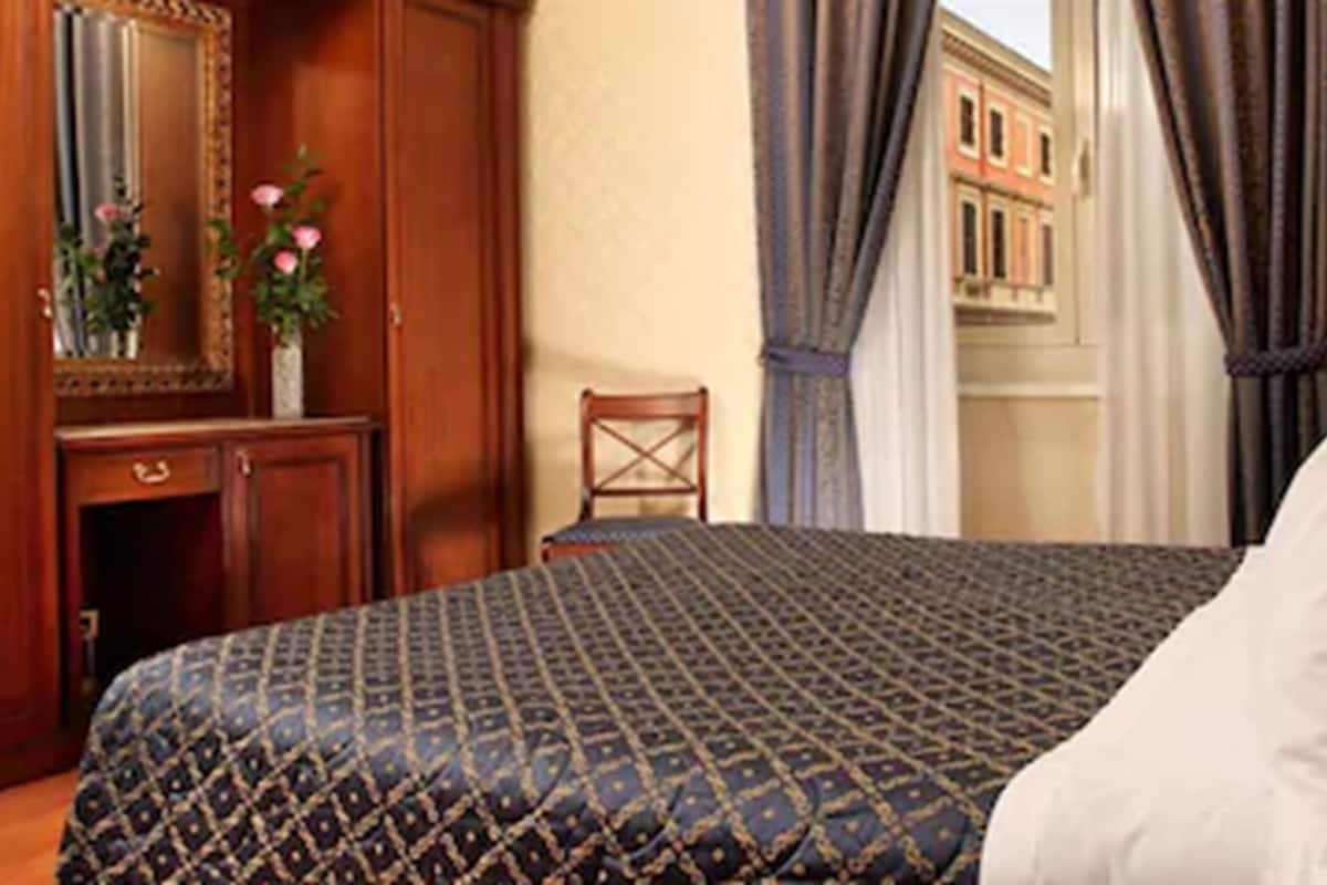 A hotel room with a bed, a wooden dresser, a chair, and a window with curtains.