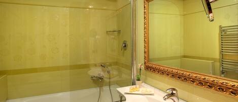 Un baño con ducha envuelta en vidrio, una bañera blanca y un tocador con espejo de marco dorado.