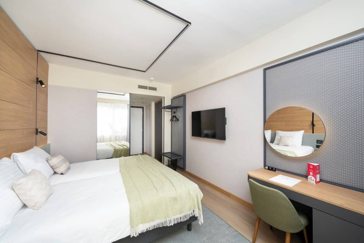 Una habitación de hotel moderna con una cama grande, un escritorio con silla, un televisor de pantalla plana y un espejo amplio.