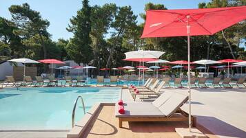 A poolside area with sun loungers and umbrellas, surrounded by trees.