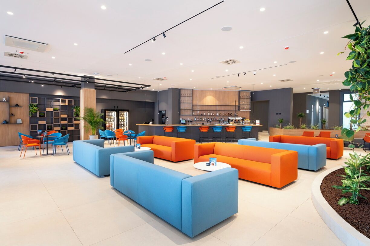 Una hall moderna con posti a sedere blu e arancioni, una reception e un'area bar.