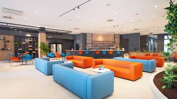 Una hall moderna con posti a sedere blu e arancioni, una reception e un'area bar.