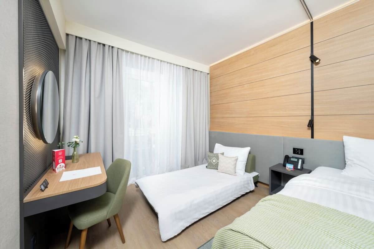 Habitación de hotel con escritorio, dos camas, mesita de noche con teléfono y un espejo grande.