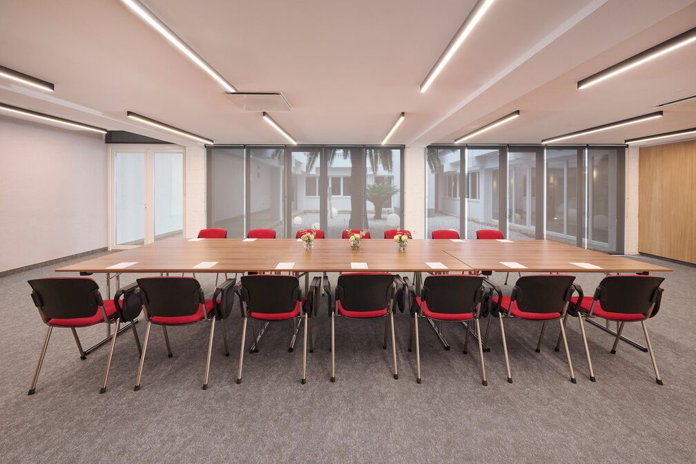 A conference room with a long table, red chairs, and large windows.