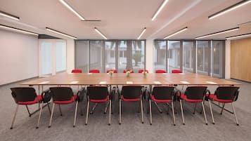 A conference room with a long table, red chairs, and large windows.