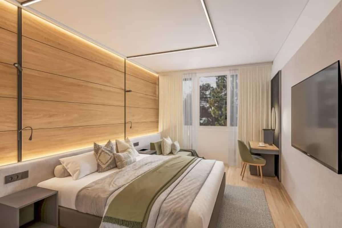 Un dormitorio moderno con cama, mesita de noche, televisor y escritorio con silla.