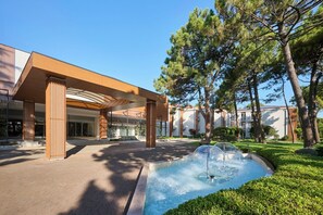 A modern building with a covered entrance, a water feature, and surrounding greenery.