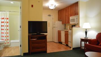 A compact kitchen with wooden cabinets, a microwave, a refrigerator, and a television on a wooden stand.