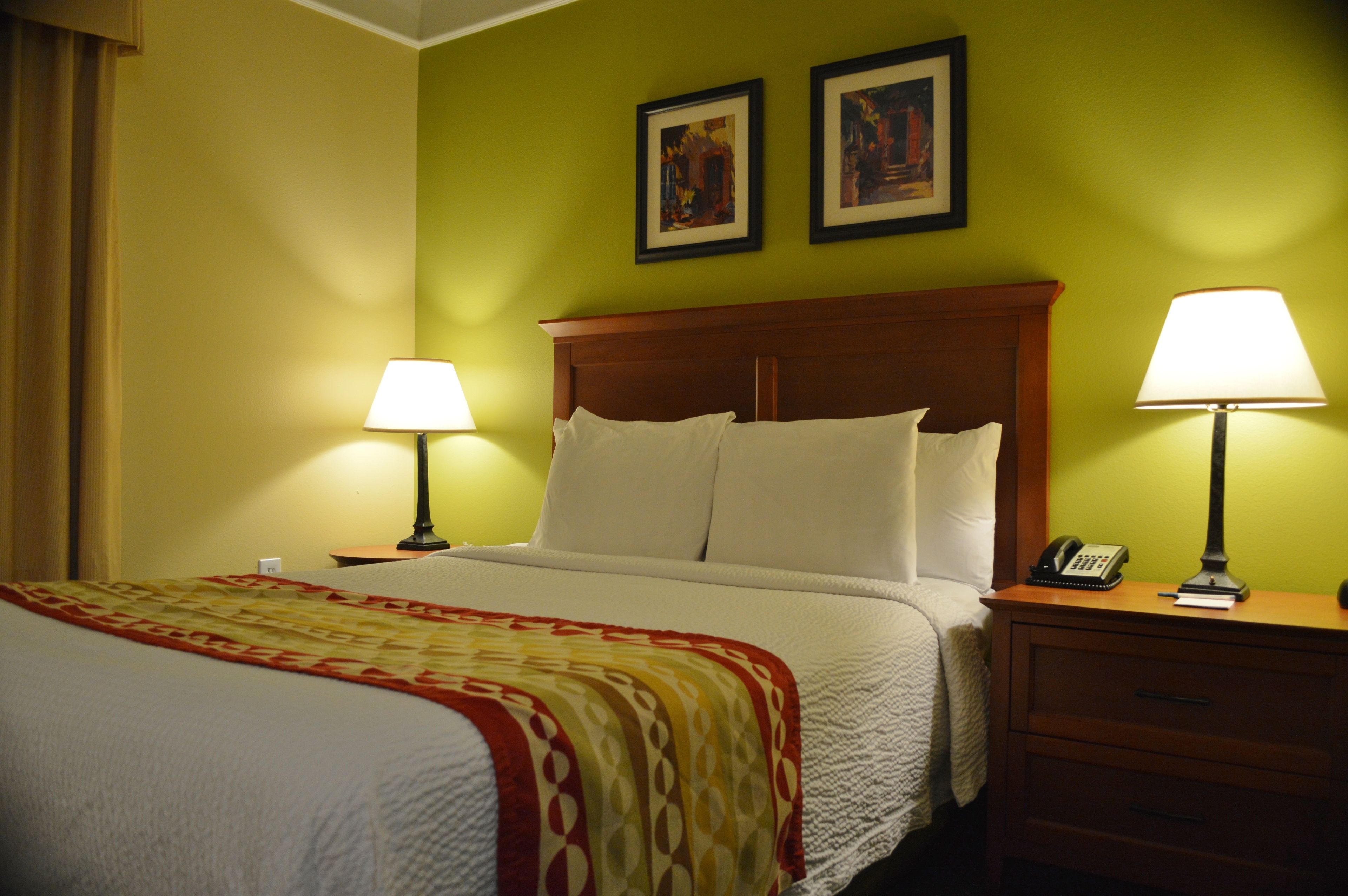 A hotel room with a bed, two bedside lamps, a nightstand with a phone, and two framed pictures on the wall.