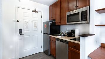 A modern kitchen with stainless steel appliances, wooden cabinets, and a white door.