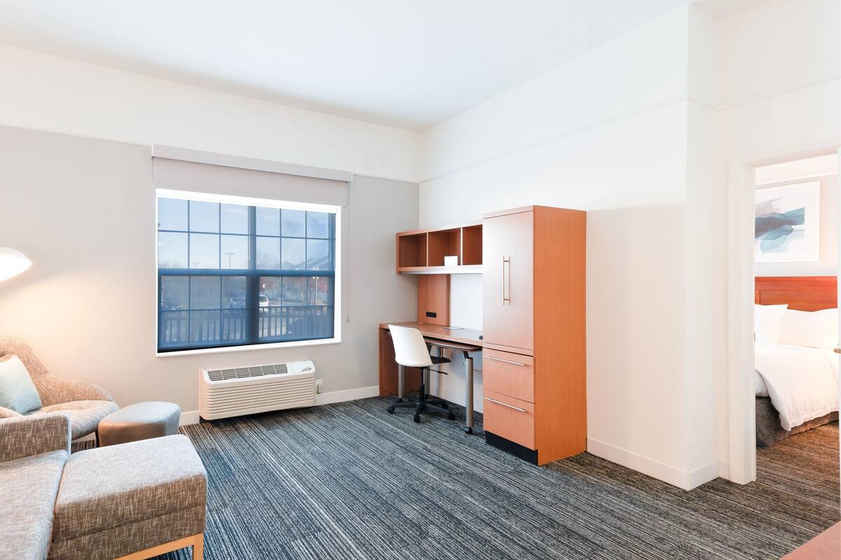 Une chambre d’hôtel avec un lit, un bureau, une chaise, un canapé, une fenêtre et un radiateur.