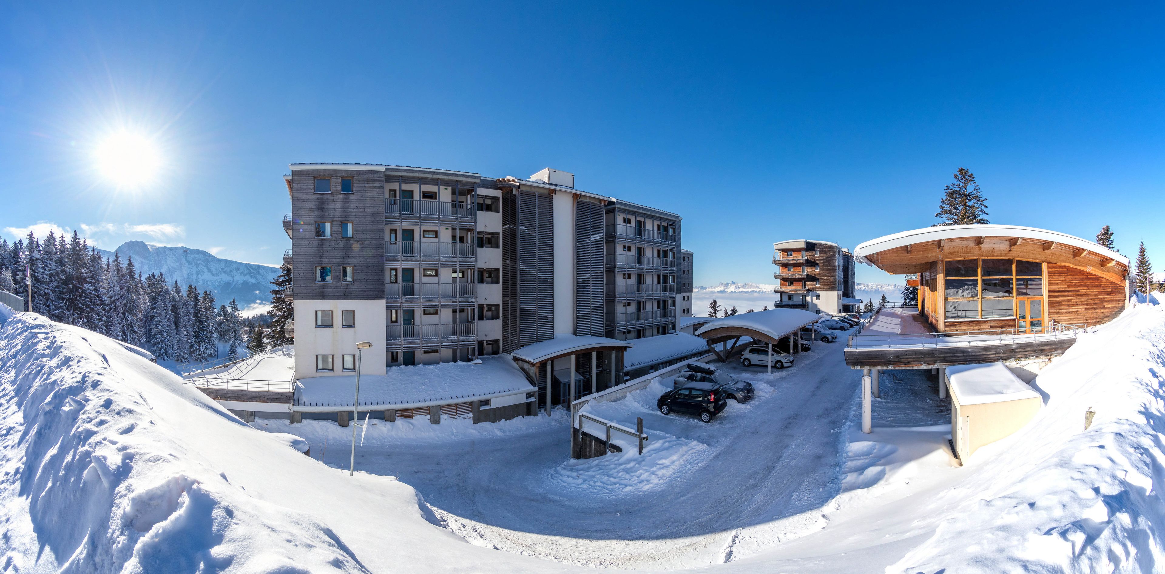 A snow-covered ski resort with modern buildings, including a multi-story hotel and a wooden structure with a curved roof.