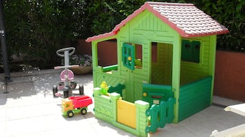 Children can play in this charming playhouse with a small entrance, windows, and door, surrounded by a low fence and lush greenery.