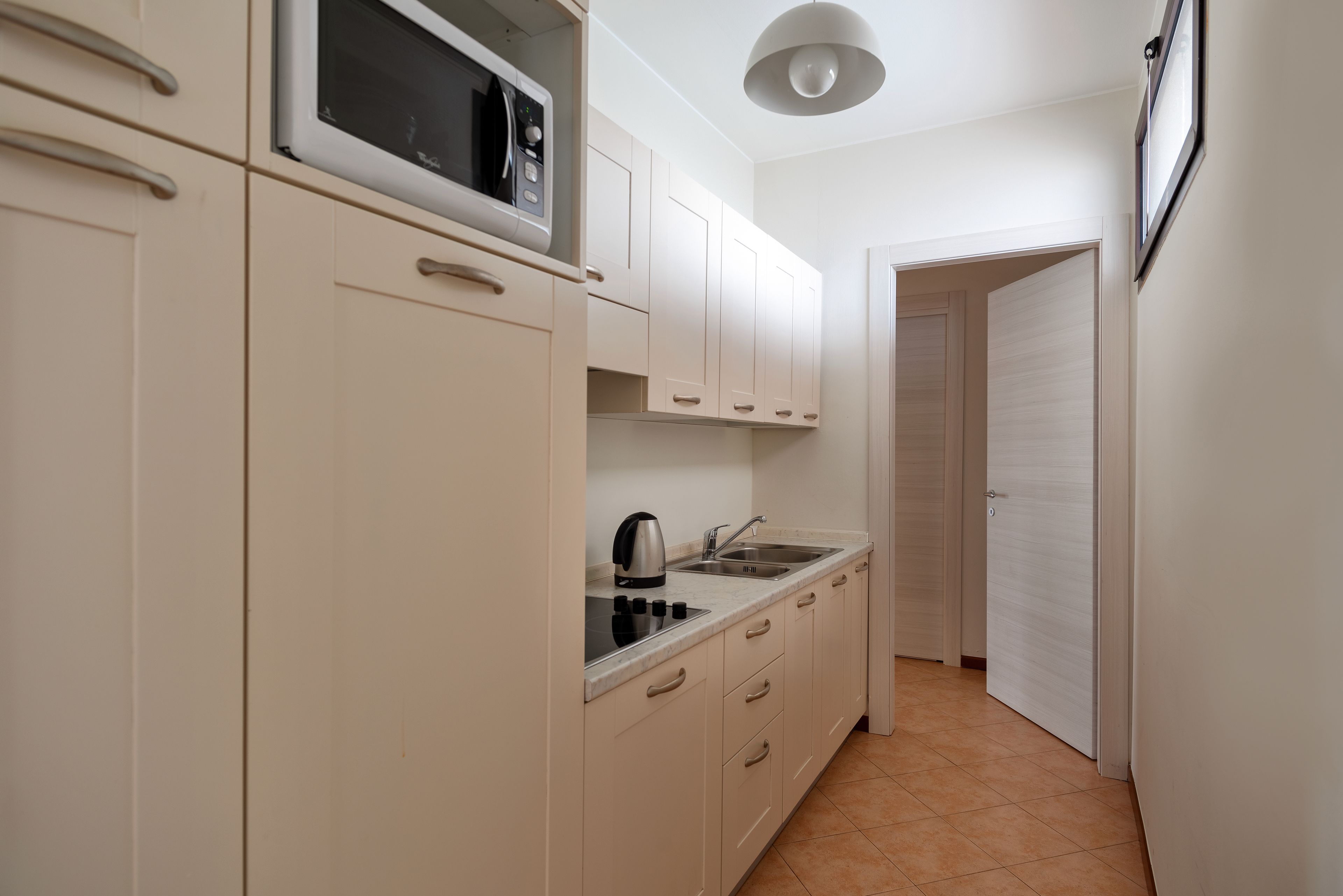 A compact kitchen with white cabinets, a microwave, a kettle, and a sink.